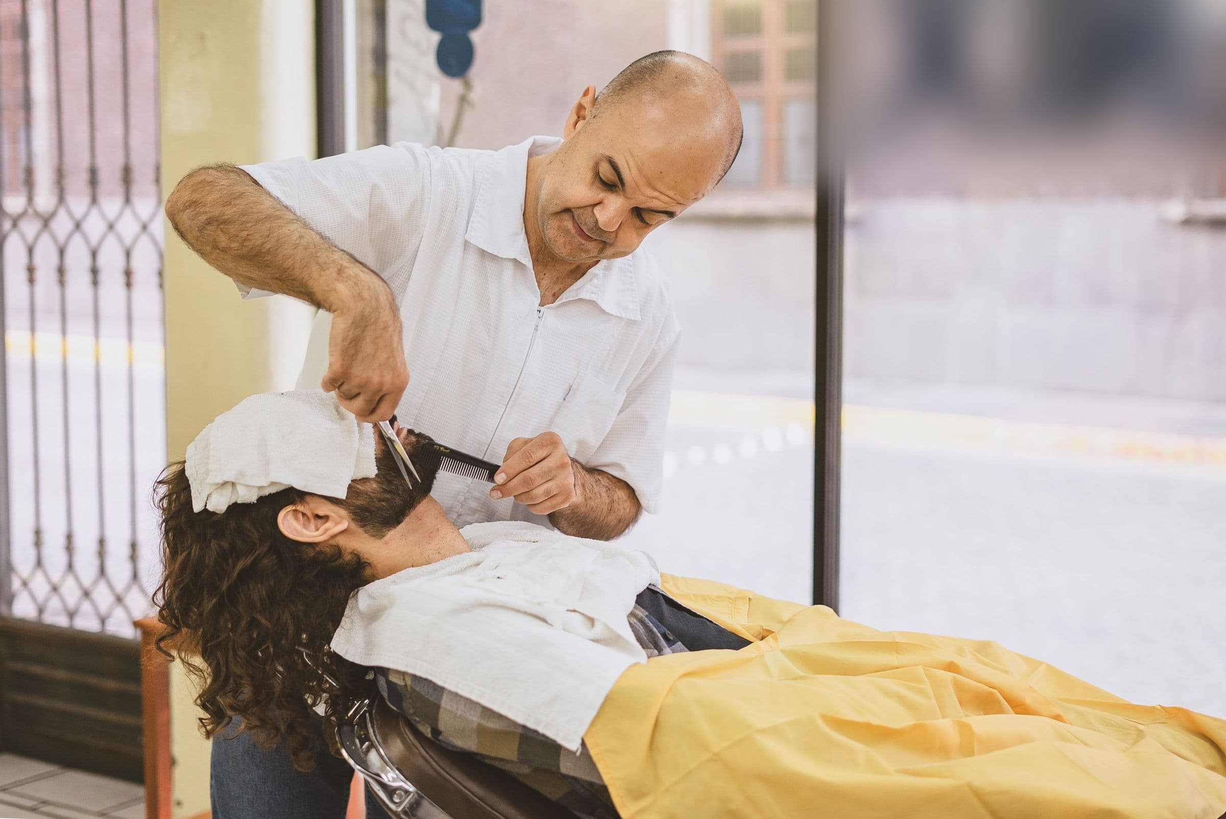 Un barbero le arregla la barba a su cliente en una barbería de barrio.
